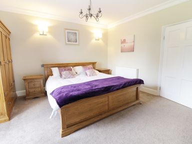 A bedroom with a wooden bed and matching furniture including bedside tables and wardrobe at Bryn Derwen in Bethesda near Caernarfon