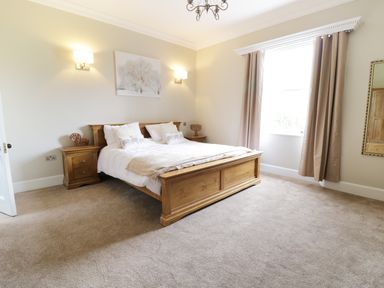 A bedroom with a wooden bed and bedside tables with lamps and a window with curtains at Bryn Derwen Bethesda near Caernarfon