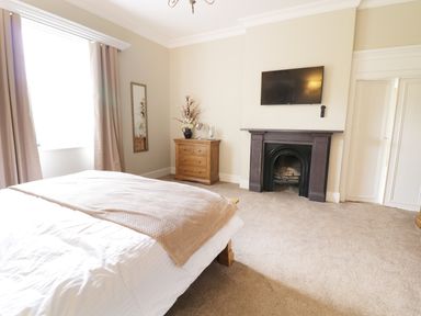 A bedroom with a bed a wooden chest of drawers a mirror a fireplace and a wall-mounted television at Bryn Derwen Bethesda near Caernarfon