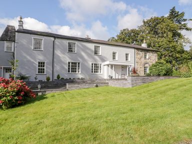 A large white two-story house with stone accents and multiple windows with a green lawn in front at Bryn Derwen Bethesda near Caernarfon