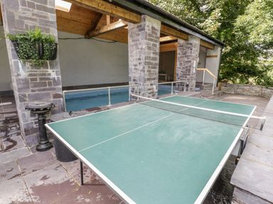 An outdoor area with a ping pong table stone pillars a small swimming pool and surrounding trees at Bryn Derwen Bethesda near Caernarfon