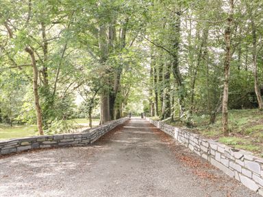 A gravel pathway lined with stone walls and trees on both sides at Bryn Derwen Bethesda near Caernarfon