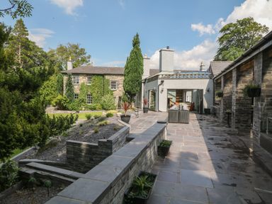 A stone patio with outdoor furniture and plants beside a stone building and a garden at Bryn Derwen in Bethesda near Caernarfon