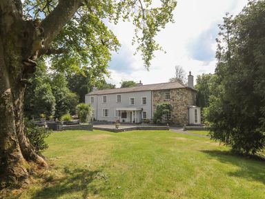 A large house with stone and white walls surrounded by grass and trees at Bryn Derwen Bethesda near Caernarfon