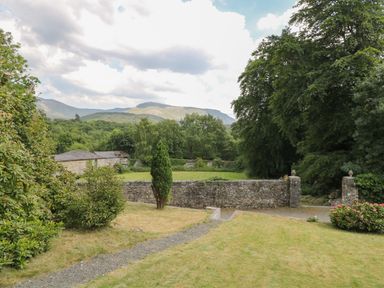 A garden with a stone wall and trees with mountains in the background at Bryn Derwen Bethesda near Caernarfon