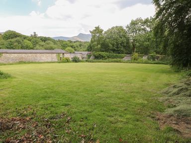A large grassy lawn bordered by stone walls and trees with mountains in the background at Bryn Derwen Bethesda near Caernarfon