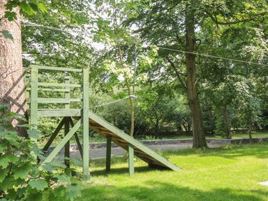 A wooden zip line platform with a grassy area and trees at Bryn Derwen in Bethesda near Caernarfon