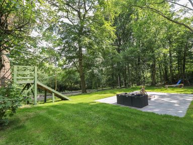 An outdoor garden area with a zip line platform slide and a paved fire pit seating area surrounded by trees at Bryn Derwen in Bethesda near Caernarfon