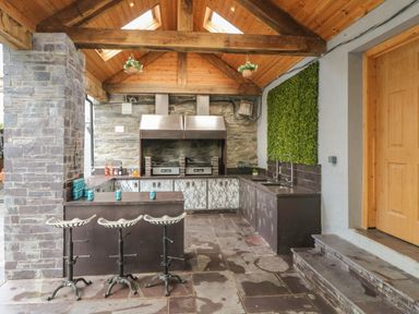 An outdoor kitchen with bar stools a grill and two sinks at Bryn Derwen Bethesda near Caernarfon