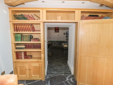 A wooden bookshelf with old books and a doorway leading to a room with bar stools and a pool table at Bryn Derwen in Bethesda near Caernarfon