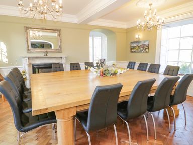 A dining room with a large wooden table surrounded by black chairs a fireplace and large window at Bryn Derwen Bethesda near Caernarfon