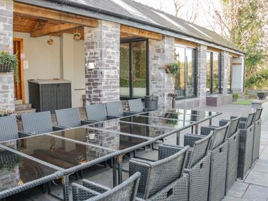 An outdoor patio with a long glass table surrounded by black wicker chairs at Bryn Derwen in Bethesda near Caernarfon