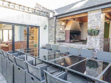 An outdoor patio with glass tables and wicker chairs next to a grill area at Bryn Derwen in Bethesda near Caernarfon