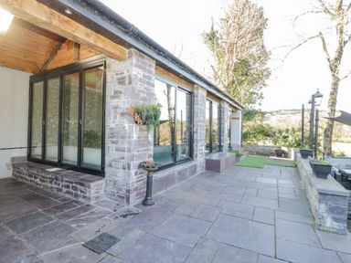 An outdoor patio with stone flooring and walls glass doors and windows and planters with greenery at Bryn Derwen Bethesda near Caernarfon