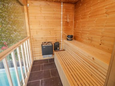 A wooden sauna room with a heater and a bucket on a bench at Bryn Derwen in Bethesda near Caernarfon