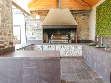 An outdoor kitchen with a grill sink cabinets and stone walls at Bryn Derwen Bethesda near Caernarfon