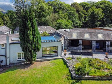 A backyard with a lawn and a patio connected to a house surrounded by trees at Bryn Derwen Bethesda near Caernarfon