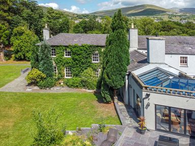 A house with ivy on one side and a glass roof extension surrounded by trees and grass at Bryn Derwen in Bethesda near Caernarfon