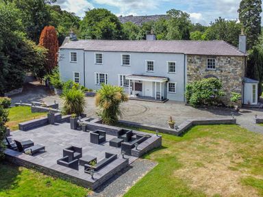 A large two-story house with a stone patio and outdoor seating area surrounded by trees at Bryn Derwen Bethesda near Caernarfon