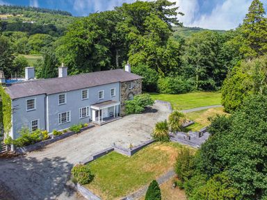 A large house with a gravel driveway surrounded by trees and grass at Bryn Derwen Bethesda near Caernarfon