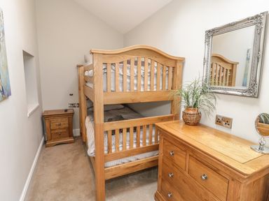 A bedroom with a wooden bunk bed wooden chest of drawers and a bedside table with a plant and mirror at Bryn Derwen Coach House Bethesda