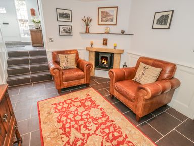 A sitting area with two brown leather armchairs facing a fireplace and a red patterned rug on a tiled floor at Bryn Derwen Coach House in Bethesda