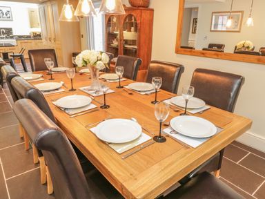 A dining room with a wooden table set with plates glasses and cutlery with leather chairs around it at Bryn Derwen Coach House in Bethesda