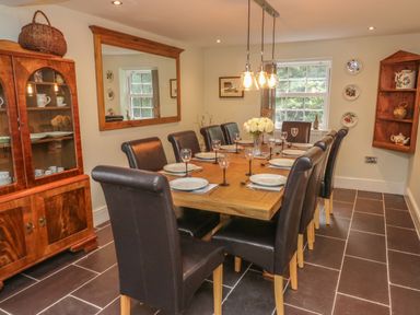 A dining room with a wooden table set for eight and a cabinet with dishes at Bryn Derwen Coach House in Bethesda