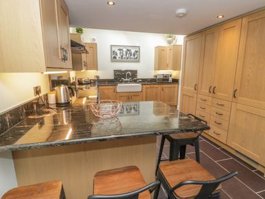 A kitchen with wooden cabinets a black countertop an island with stools a kettle toaster and a microwave at Bryn Derwen Coach House Bethesda