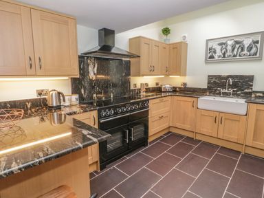 A kitchen with black appliances wooden cabinets black marble countertops and a farmhouse sink at Bryn Derwen Coach House in Bethesda