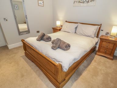 A bedroom with a wooden bed with white bedding and rolled towels on top with two wooden nightstands with lamps and a tall mirror on the wall at Bryn Derwen Coach House Bethesda