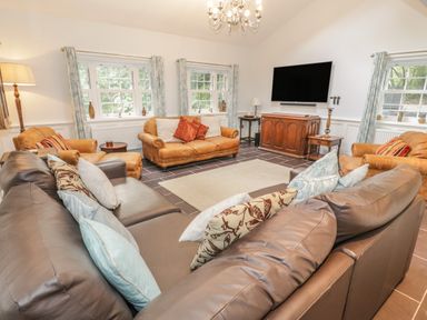 A living room with multiple leather sofas facing a wall mounted television at Bryn Derwen Coach House in Bethesda