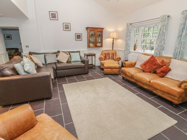 A living room with two brown leather sofas an armchair a cream rug and a window with curtains at Bryn Derwen Coach House in Bethesda