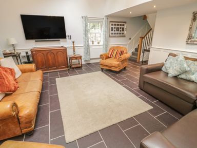 A living room with leather sofas an armchair a large rug and a wall mounted television at Bryn Derwen Coach House in Bethesda