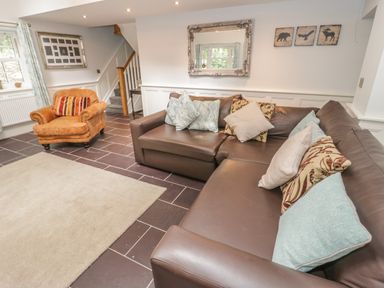 A living room with a brown leather sofa, an orange armchair, cushions, a beige rug, wall mirror, and framed pictures at Bryn Derwen Coach House in Bethesda