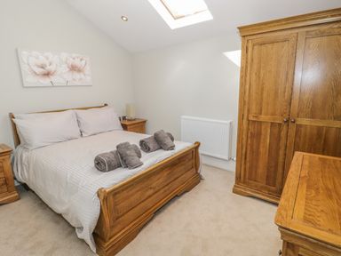 A bedroom with a wooden bed frame and matching furniture at Bryn Derwen Coach House in Bethesda