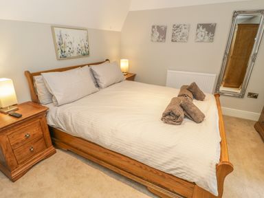A bedroom with a wooden bed with white bedding two bedside tables with lamps a wall mirror and framed floral artwork at Bryn Derwen Coach House Bethesda