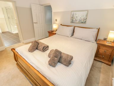 A bedroom with a wooden bed with folded towels on it two bedside tables with lamps and an open door leading to a bathroom at Bryn Derwen Coach House in Bethesda