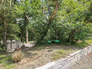 Two green swings hanging from a tree near a paved outdoor seating area surrounded by trees at Bryn Derwen Coach House in Bethesda