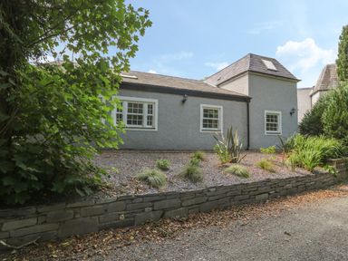 Exterior view of a gray house with white window frames surrounded by plants and trees at Bryn Derwen Coach House in Bethesda