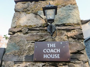 A stone wall with a lantern and a sign that reads The Coach House at Bryn Derwen Coach House in Bethesda