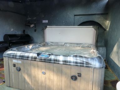 A hot tub filled with water inside a room with blue walls and a barbecue grill in the corner at Bryn Derwen Coach House in Bethesda