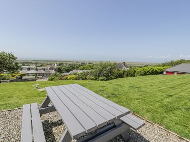 A picnic table on a gravel area with green lawn and houses in the background at Bryn Coch Bach in Dyffryn Ardudwy