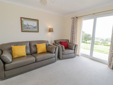 A living room with two leather sofas and cushions a floor lamp a painting on the wall and sliding glass doors with curtains at Bryn Coch Bach in Dyffryn Ardudwy
