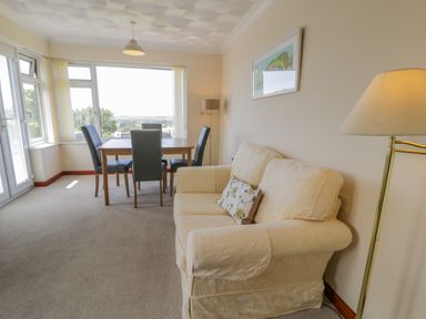 A sitting area with a beige sofa and dining table with four chairs near large windows at Bryn Coch Bach in Dyffryn Ardudwy