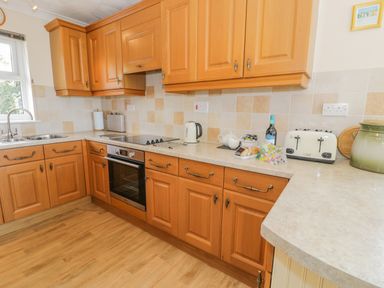 A kitchen with wooden cabinets an electric oven a toaster and various kitchen items on the countertop at Bryn Coch Bach in Dyffryn Ardudwy