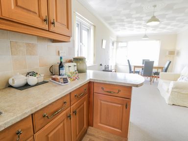 A kitchen counter with a teapot toaster and wine bottle and a dining table with chairs in the background at Bryn Coch Bach in Dyffryn Ardudwy