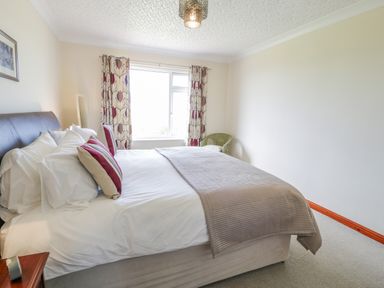 A bedroom with a bed white sheets cushions curtains window and a chair at Bryn Coch Bach in Dyffryn Ardudwy