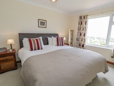 A bedroom with a double bed striped cushions bedside tables and a window with patterned curtains at Bryn Coch Bach in Dyffryn Ardudwy