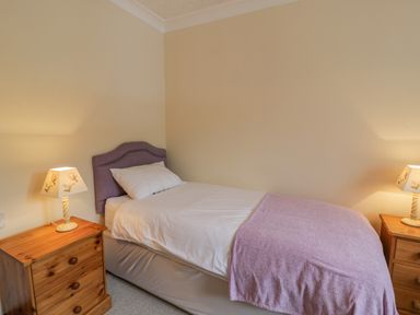 A single bed with white bedding and a purple blanket between two wooden bedside tables with lamps at Bryn Coch Bach in Dyffryn Ardudwy